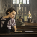 Fleabag is in a church sitting in one of the pews, turning backwards to look at the camera sneakily.